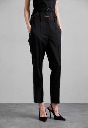 Black tailored trousers with a sleek design, featuring a high waist, pleated front, and tapered leg, paired with black high-heel shoes.