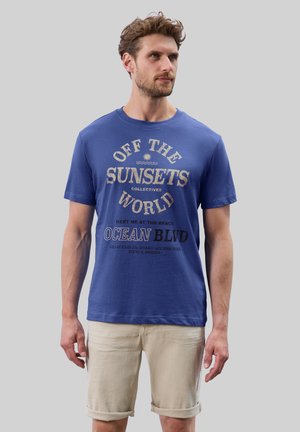 Blaues Baumwoll-T-Shirt mit kurzen Ärmeln. Mit Textgrafiken in verschiedenen Schriftgrößen und Farben: hellbeige und marineblau, vor einem blauen Hintergrund.
