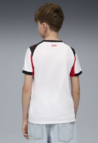 Maglia sportiva bianca con dettagli neri e rossi, maniche corte e collo rotondo. Logo "MILAN" in rosso sul retro vicino al colletto.