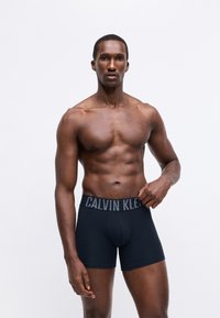 Černé boxerky od Calvin Klein s logem na pásku, vyrobené z hladké tkaniny, s těsným střihem a délkou do poloviny stehna.