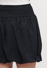 Svart skjørt med elastisk linning, med en samlet design og teksturert stoff, som gir et flytende utseende.