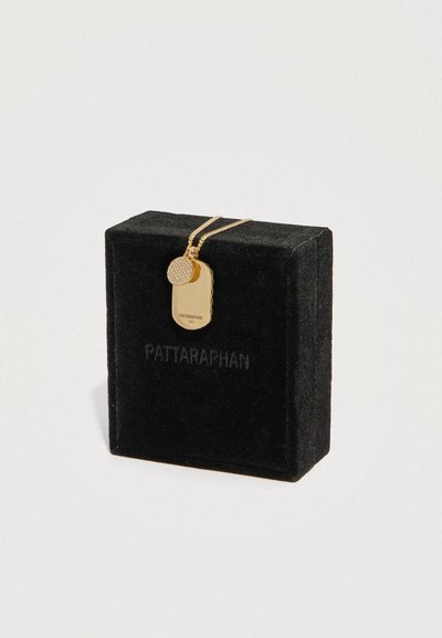 Šperkovnica z čierneho zamatového materiálu s náhrdelníkom so zlatým príveskom na psí známke zo 14-karátového zlata a malým okrúhlym diamantom na retiazke položená cez škatuľku.