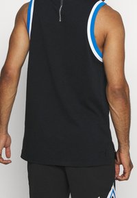 Man med svart ärmlös sporttröja med blå och vit kant samt matchande svarta shorts med geometrisk blå och vit design.