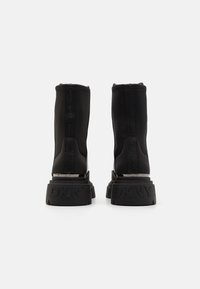 Svarte ankelstøveler laget av elastisk materiale, med en tykk, teksturert såle med preget "DKNY"-merke og et stilrent design.
