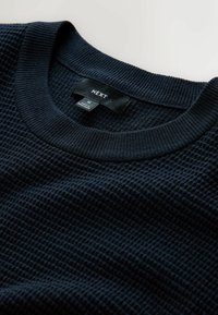 Marineblauer, strukturierten Pullover mit einem gerippten Rundhalsausschnitt. Sichtbares Etikett mit der Marke 'NEXT' und Größe 'M'. Weicher, gewebter Stoff.