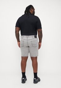 Zwart T-shirt met korte mouwen, gecombineerd met grijze denim shorts met achterzakken en een zwarte tailleband patch. Model draagt zwarte sokken en sneakers.
