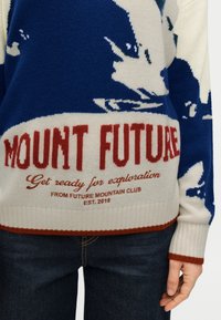 Πλεκτό πουλόβερ σε κρεμ χρώμα με μπλε μοτίβο βουνών. Διαθέτει κόκκινο κείμενο "MOUNT FUTURE" και rib μανσέτες και τελείωμα. Ιδανικό για καθημερινή χρήση.