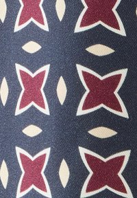 Marineblauer Stoff mit einem wiederholten geometrischen Muster aus roten und cremfarbenen Formen, einschließlich überkreuzter Figuren und Mandeln, mit einer glatten Textur.