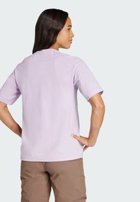 Svetlofialová tričko s krátkym rukávom a okrúhlym výstrihom, hladká textúra a švové detaily na pleciach, spárované s hnedými šortkami.
