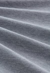 Sivý textil s textúrovaným povrchom, ktorý má výrazné diagonálne skladby a jemne melírovaný vzor. Materiál vyzerá odolne a je tkaný.