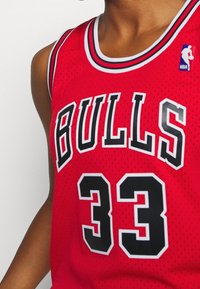 Punainen koripallopaita, jossa on mustalla kirjoitettu "BULLS" ja valkoisella ääriviivalla varustettu numero "33". Valmistettu verkkomateriaalista ja pyöreäkaula-aukko.