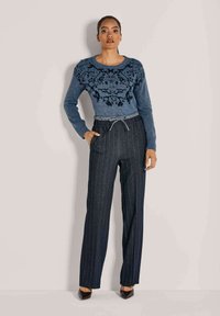 Blauw gebreid truitje met zwart bloemenpatroon op het lijfje, gecombineerd met hoge, gestreepte broek en hakken.