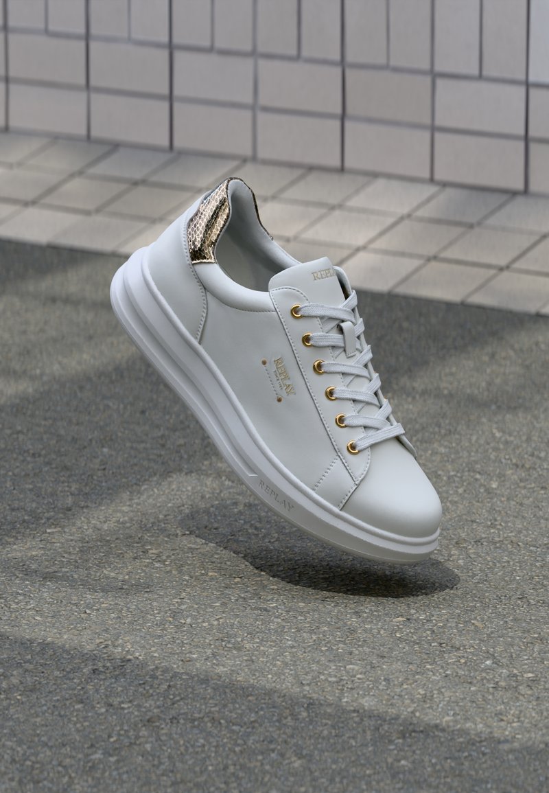 Sneaker in pelle bianca con occhielli dorati, caratterizzata da un'accenno dorata testurizzata sul tallone. Superficie liscia e design con punta arrotondata.