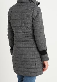 Zwarte en grijze geruite donsjacquet met verticale stiksels, hoge kraag en zwarte ribstof manchetten. Middelgrote lengte, duurzaam materiaal.