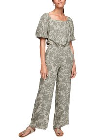 Femme portant une tenue deux pièces avec des manches bouffantes et un pantalon ample à motif floral vert et beige, assortie à des sandales beiges.