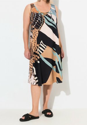 Femme portant une robe sans manches, longueur au genou, avec des motifs abstraits multicolores et des sandales noires tissées à ouverture sur les orteils, à enfiler.