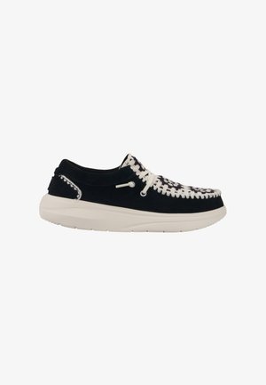 Chaussure en suède noir avec un motif tissé blanc sur le bout et des lacets blancs. Elle présente une semelle en caoutchouc blanc rembourrée et des détails de couture.