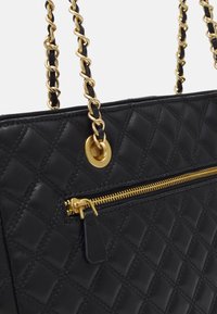 Borsa a mano in pelle nera trapuntata con tracolla in catena dorata, tasca con zip e zip dorata, e dettaglio con occhiello metallico.