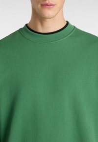 Sudadera verde de cuello redondo hecha de una tela suave, con un diseño sencillo y cuello acanalado. Sin patrones o adornos visibles.
