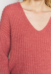 Pullover rosa a maglia con scollatura a V profonda, texture a coste e maniche lunghe, che mette in risalto un aspetto morbido e accogliente.