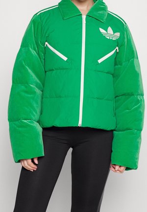 Chaqueta acolchada verde con cremallera blanca, bolsillos en el pecho en ángulo, logo de Adidas en el pecho izquierdo, combinada con leggings negros.