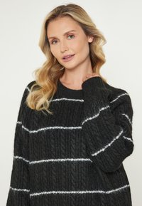 Pulover negru tricotat cu dungi orizontale albe, material texturat, guler rotund și croială largă. Prezintă mâneci lungi și detalii ribelate.