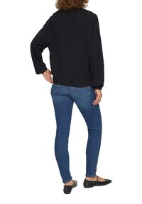 Schwarzer, strukturierten Pullover mit langen Ärmeln, kombiniert mit blauen, enganliegenden Jeans und schwarzen Ballerinas. Der Pullover hat eine lässige Passform.