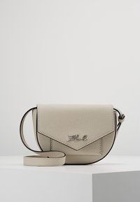 Beige nahkainen olkalaukku, jossa on teksturoitu pinta, kulmikas läppä, musta reunus ja hopeanvärinen logo. Säädettävä hihna mukana.