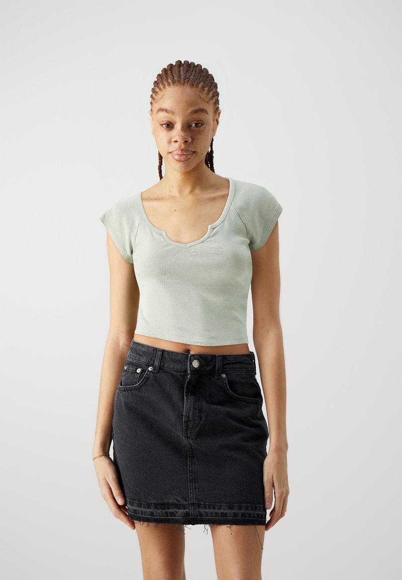Lys grøn cropped top med rund halsudskæring og korte ærmer, parret med en sort denimnederdel med frynset kant og forlommer.