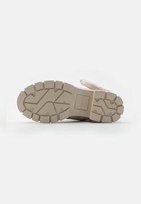 Suola di una scarpa con superficie in gomma texture, caratterizzata da un colore beige chiaro e un motivo scanalato per trazione e aderenza.