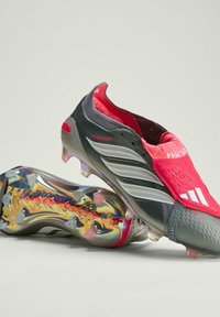 Sort- og røde fodboldstøvler med en tekstureret overdel, sølvstriber og en gennemsigtig, iriserende sål med synlige knopper. Har et tætsiddende design.