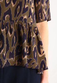 Oliwkowa bluzka z fasonem peplum, w niebiesko-beżowy wzór lamparta. Miękki, lekki materiał z krótkimi rękawami.