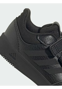 Sneaker atletico nero con tomaia in pelle texurizzata, dettagli in mesh, colletto imbottito e suola in gomma con tre strisce parallele.