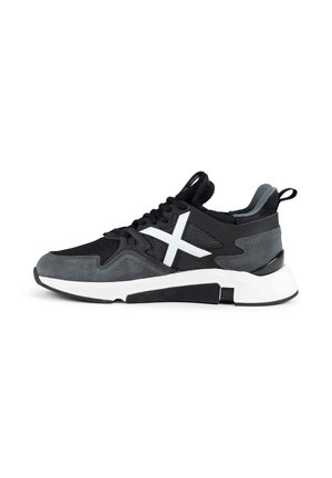 Sneaker nero e grigio con suola bianca spessa e logo X bianco sul lato, lacci neri e linguetta sul tallone su sfondo bianco.