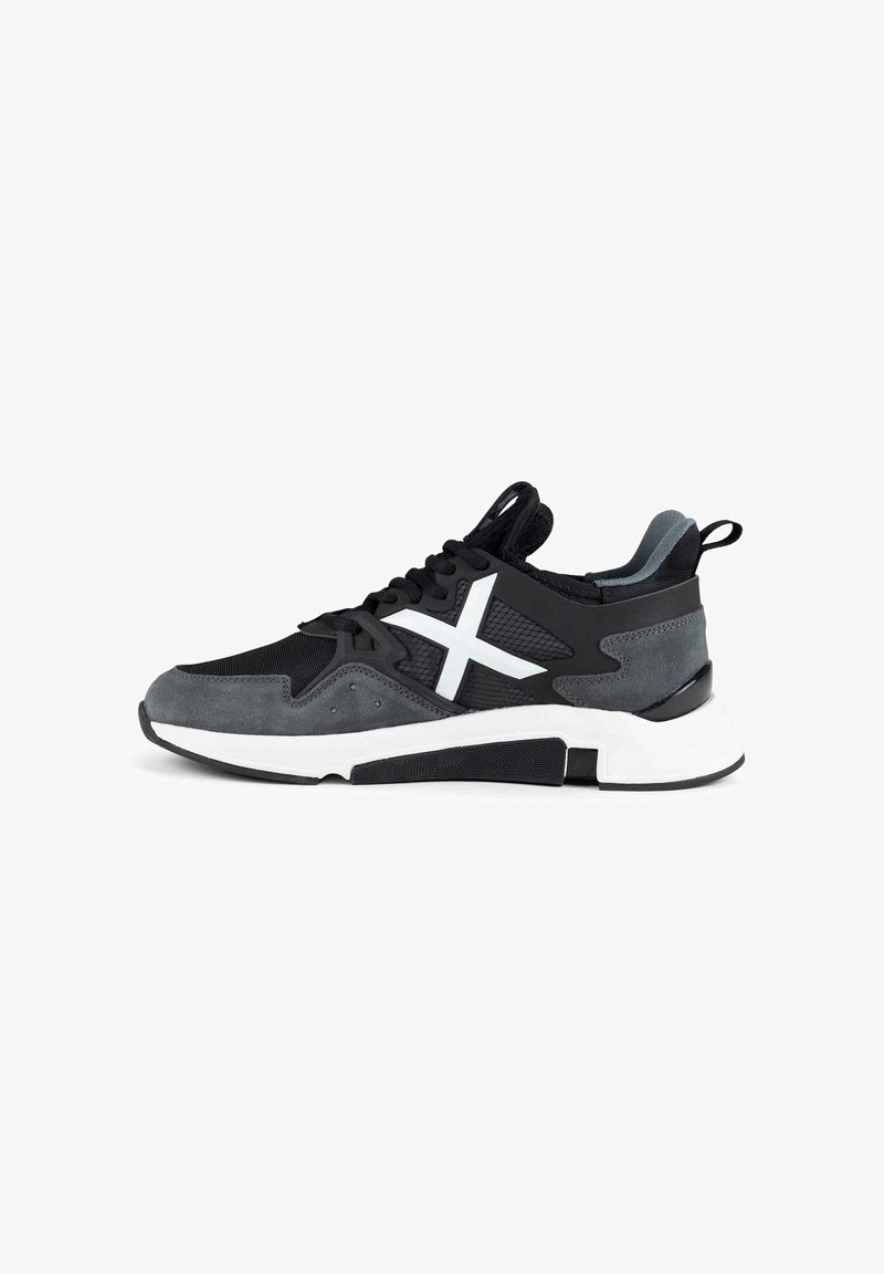 Baskets noires et grises avec semelle blanche épaisse et logo X blanc sur le côté, lacets noirs et languette au talon sur fond blanc.