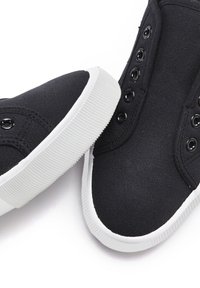 Schwarze Leinensneaker mit weißen Gummisohlen, ausgestattet mit schwarzen Ösen, strukturierten Oberflächen und einem runden Zehendesign.