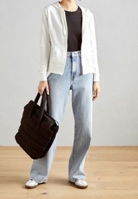 Felpa zip-up grigia chiara, maglietta nera attillata, jeans a vita alta blu chiaro e borsa tote imbottita marrone scuro; ai piedi delle sneakers bianche.