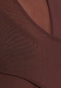 Hnědá síťovina s hlubokým výstřihem do V a jemnou texturou, s čistým šitím podél výstřihu a lemů pro bezproblémový vzhled.