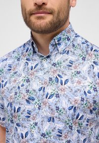 Camicia a maniche corte con un motivo floreale arricchito da tonalità di blu, verde e beige. Realizzata in un tessuto leggero, con colletto e chiusura a bottoni.