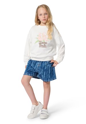 Weißer Pullover mit floralem Design und "Kenzo Paris"-Schriftzug, kombiniert mit einem blauen Jeansrock mit abstrakten Mustern und weißen Klettverschluss-Sneakern.
