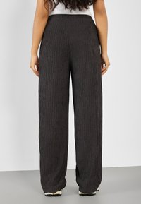 Zwarte, wijde broek van textuurstof met verticale plooien, voorzien van een hoge taille en een elastische tailleband.