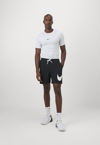 Valkoinen lyhythihainen urheilupaita, jossa on musta Nike-logo, yhdistetty mustiin shortseihin, joissa on valkoinen Nike-swoosh ja joustava vyötärö. Valkoiset lenkkarit.