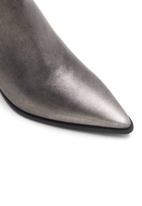 Zapato de punta metálico plateado con textura suave y diseño elegante, con una suela negra. La vista en primer plano destaca el acabado.