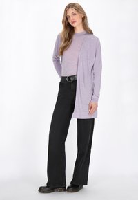 Lichtpaarse lange mouwen cardigan gelaagd over een lichtpaarse top, gecombineerd met hoge taille zwarte wijde broek en zwarte enkellaarsjes.
