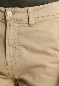 Beige bomullbyxor med en mjuk textur, som har synliga knappar och sömnadsdetaljer fram och på fickorna.