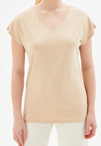 Beige V-ringad T-shirt tillverkad av mjukt tyg med korta ärmar, som kännetecknas av en avslappnad passform och slät textur. Inga synliga mönster eller detaljer.