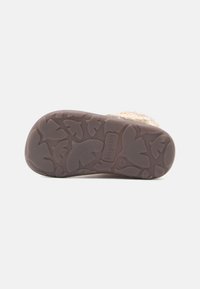 Brun gummisåle med bladmønstrede dekksåler og preget merkevarelogo. Overdelen har mykt beige materiale som sikrer komfort og varme.
