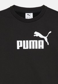 Melna kokvilnas T-krekls ar lielu baltu "PUMA" logotipu, kas attēlo lecošu pumā, ar apaļu kakla izgriezumu un īsām piedurknēm.