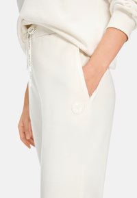 Weiße Baumwoll-Jogginghosen mit einer Seitentasche und einem strukturierten, runden Logo. Tunnelzug am Bund, mit einer glatten, weichen Textur.