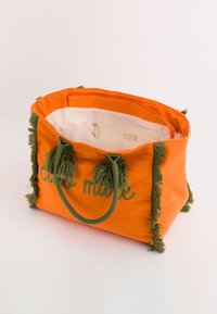 Gran bolso tote de lona naranja grande con borlas verdes, cuenta con un bolsillo interior con cierre y texto bordado, asas de cuerda duraderas.